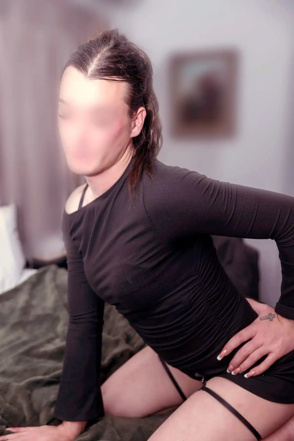 London in a black top, kneeling on a bed with a hand on her hip